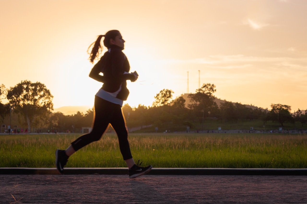 Woman following a morning routine for weight loss, running outdoors at sunrise