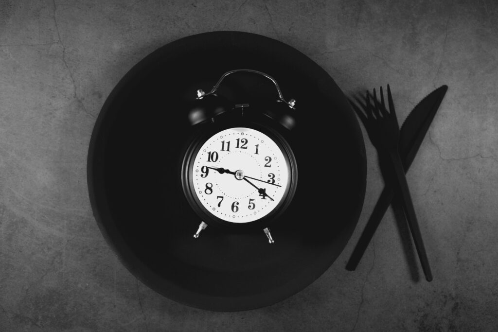 alarm clock on empty plate with cutlery showing intermittent fasting eating window concept